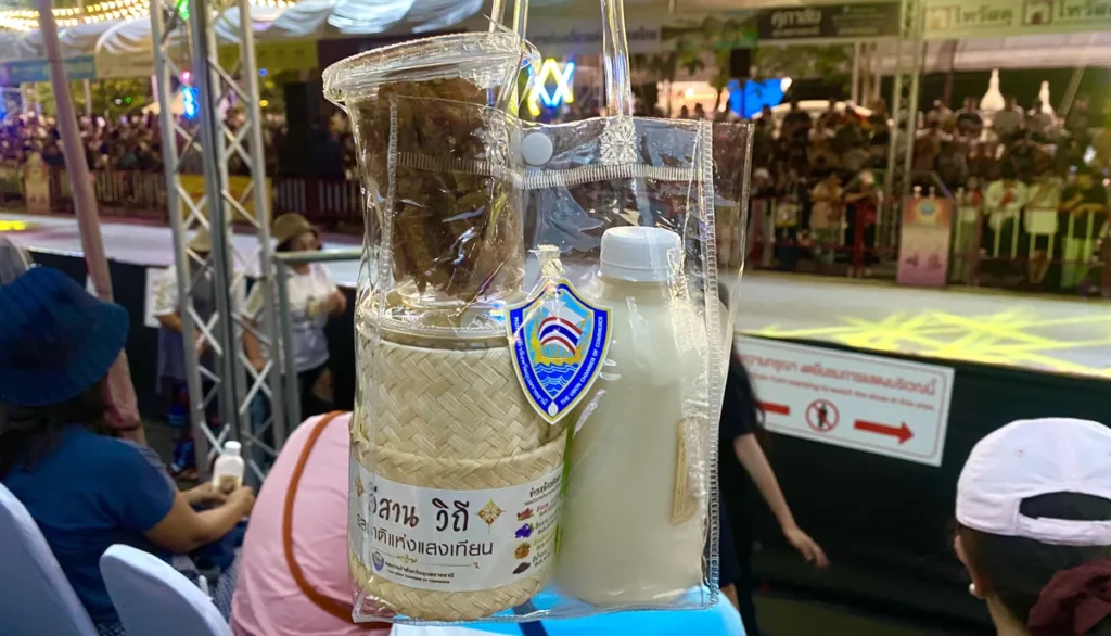 A transparent bag containing a traditional bamboo sticky rice container and a bottle of milk at the Ubon Ratchathani Candle Festival grandstand.