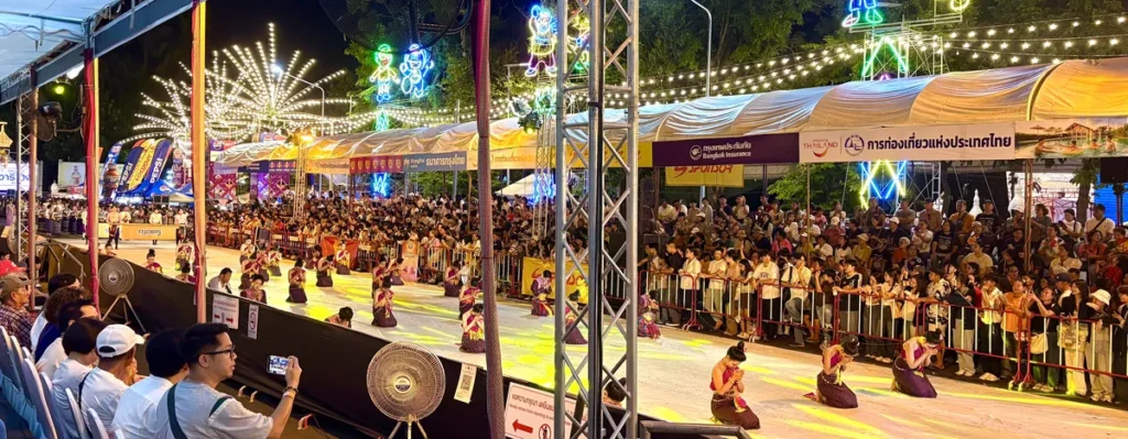 Traditional Isan dancers performing on an illuminated street during the night parade at the Ubon Ratchathani Candle Festival.