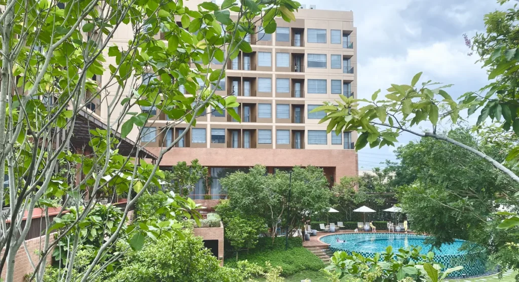 A modern swimming pool surrounded by green trees and a large garden at Centara Ubon hotel.