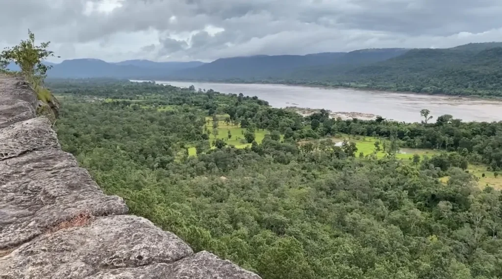 Panoramic view of the Mekong River winding through dense green forests and rolling hills from the cliffs of Pha Taem in Ubon Ratchathani Province, Isaan.