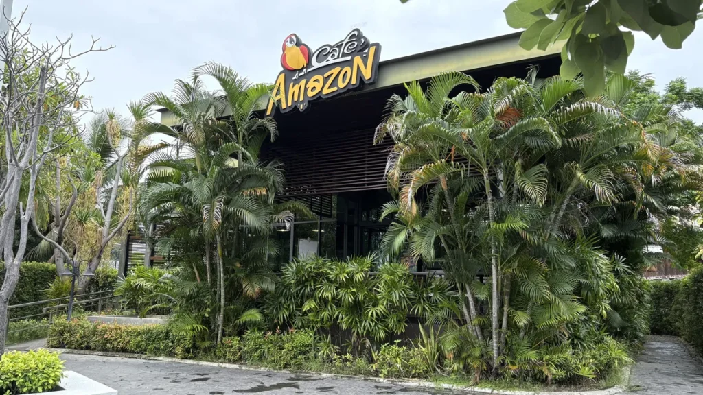 A modern air-conditioned Cafe Amazon coffee shop surrounded by green palm trees at a PTT station in Isaan.