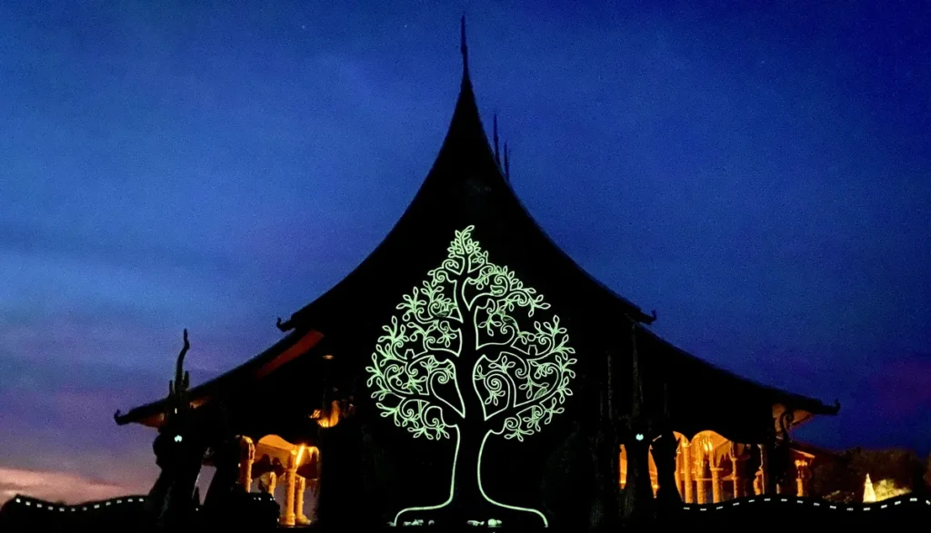 Fluorescent tree of life mural glowing green on the temple facade at Wat Sirindhorn Wararam in Ubon Ratchathani Province, Isaan.
