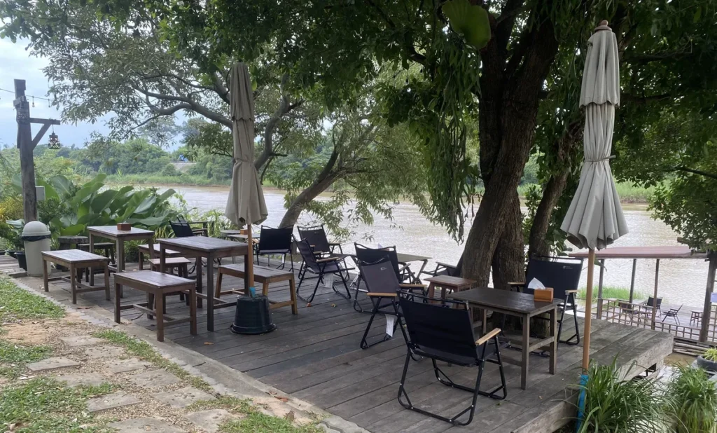 Isaan travel guide photo showing the spacious wooden riverside deck, outdoor tables and comfortable seating at Baanrimmoon Café.