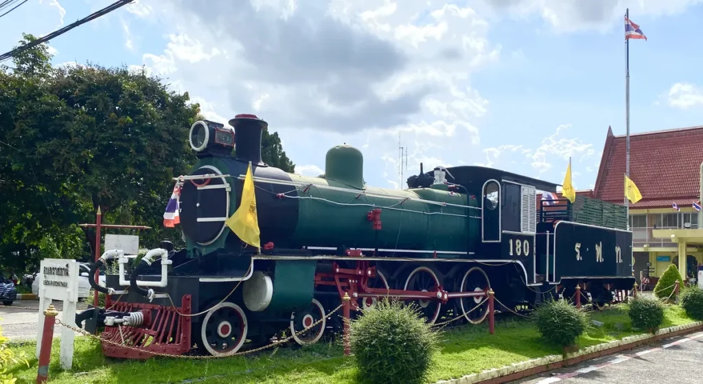 A historic green and black steam train locomotive monument displayed outside the Ubon Ratchathani railway station.
