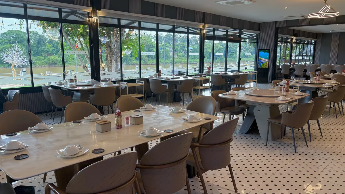 Premium air-conditioned restaurant interior with structured modern seating and large glass windows overlooking the Mun River in Ubon Ratchathani, Isaan.