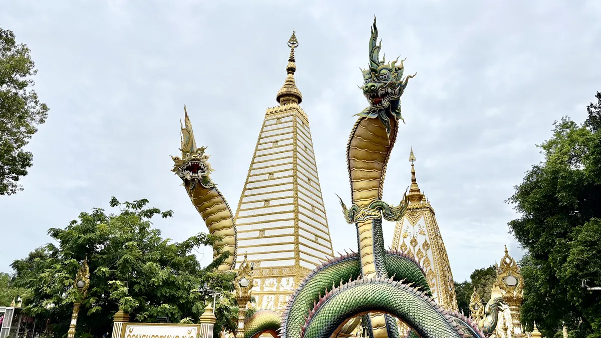 The majestic green and gold Naga statues in front of the white chedi at Wat Phra That Nong Bua.