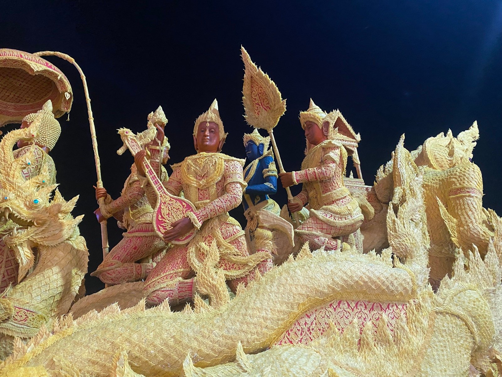 An intricate, illuminated golden beeswax sculpture float depicting Buddhist mythological figures during the night procession of the Ubon Ratchathani Candle Festival.