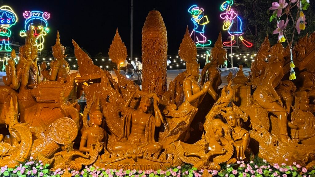 An illuminated wax sculpture float gliding through the dark streets during the evening parade of the Ubon Ratchathani Candle Festival.